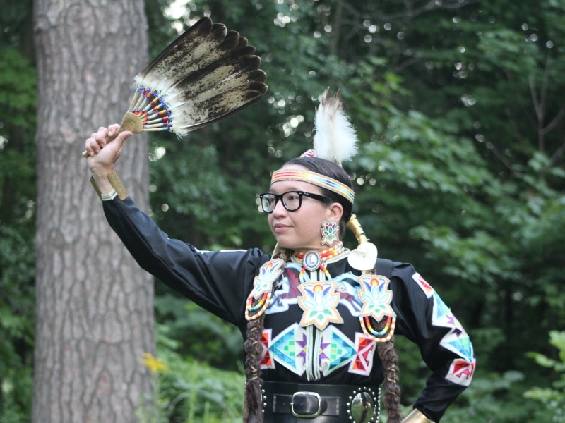 Kelli Marshall dressed in jingle dress regalia holds an eagle feather over her head