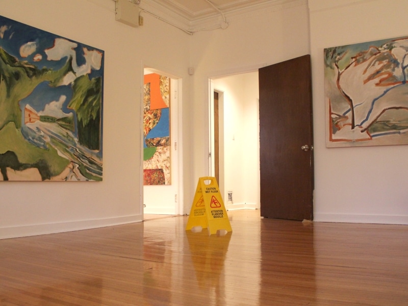 A 'Caution floor slippery' sign sits between two paintings at Sadleir House.