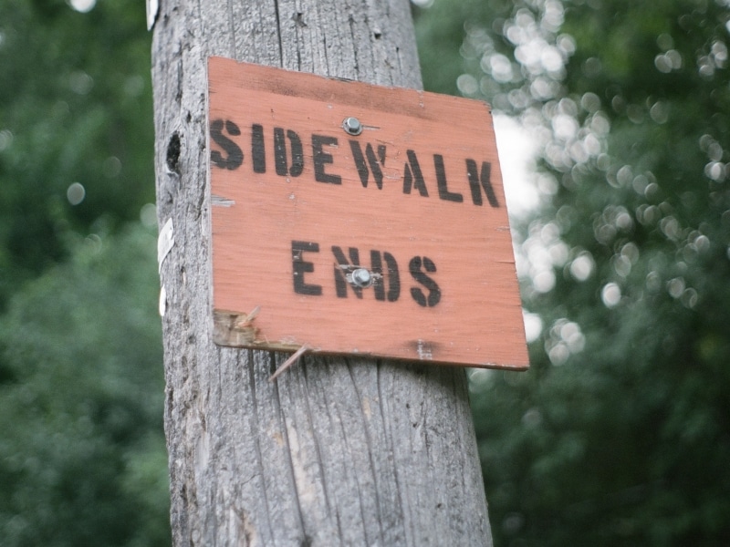 The words "sidewalk ends" are written in black lettering on a small, orange sign affixed to a telephone pole.