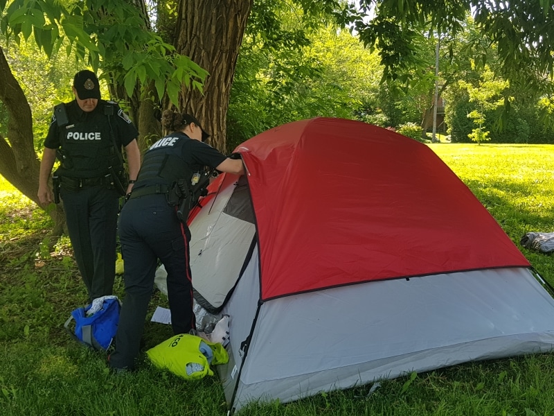 A Peterborough police officer opens the flap of a tent in a city park, as another officer stands beside her.