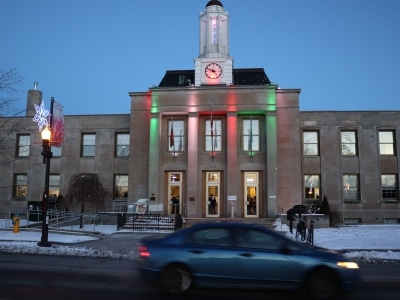 Photo shows Peterborough city hall lit up in the evening, with a car passing on the street in front.