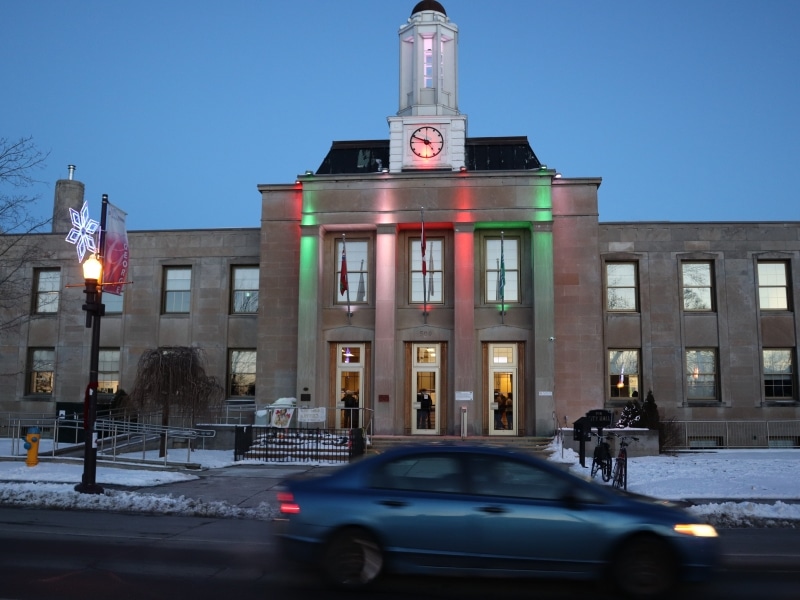 Photo shows Peterborough city hall lit up in the evening, with a car passing on the street in front.