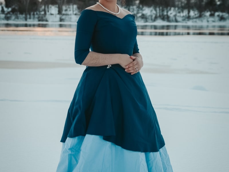 Photo shows a woman in a dress standing in front of the frozen Otonabee River