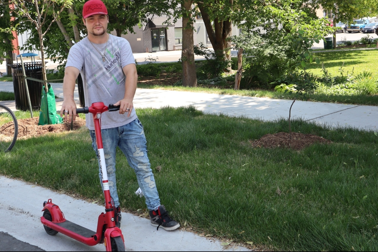 Photo shows a man holding a kick scooter on the side of Bethune Street.