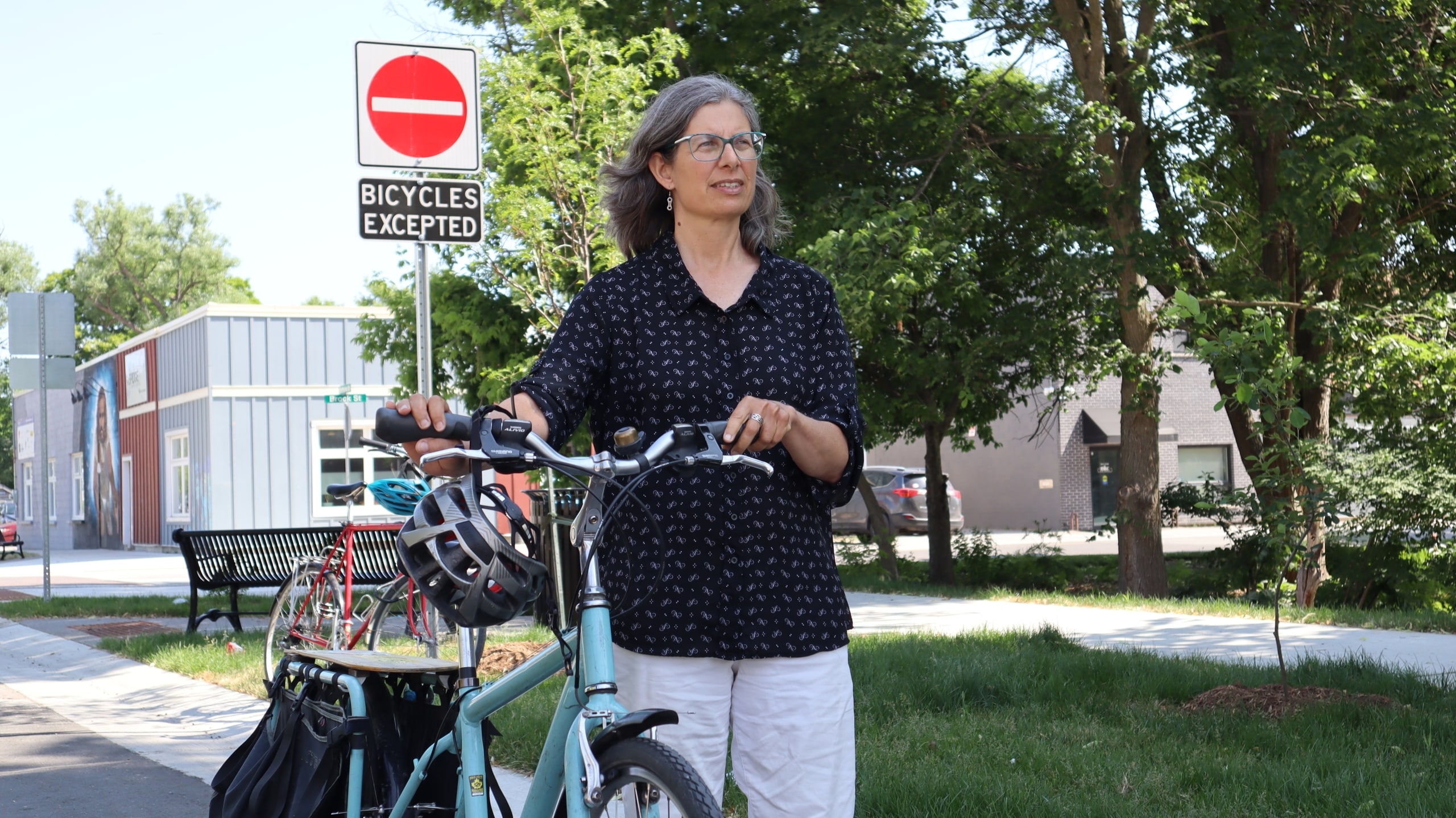 Photo shows cyclist Sue Sauve standing beside her bicycle on Bethune Street, in front of a sign that says "bicycles excepted"