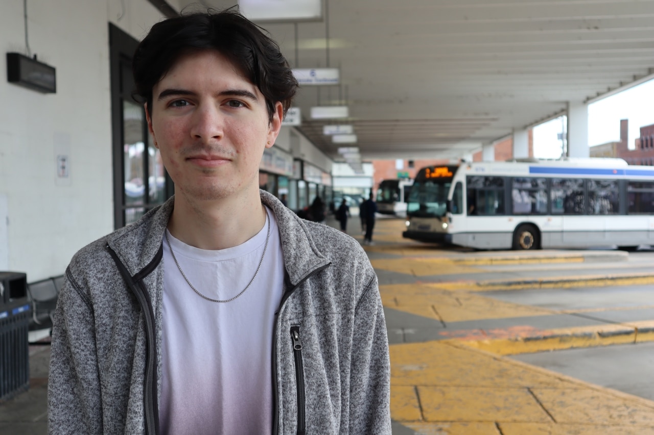 Bus rider Noah Edwards poses for a photo at Peterborough's downtown transit terminal, as a bus pulls in behind him.
