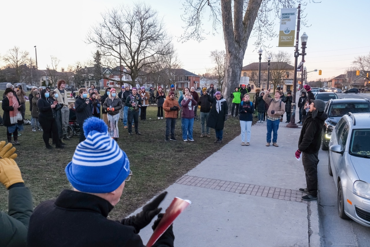 A group of people stand in Confederation Square, one of them smiles while holding a high sign that reads "you do not need a permit to do what is right."