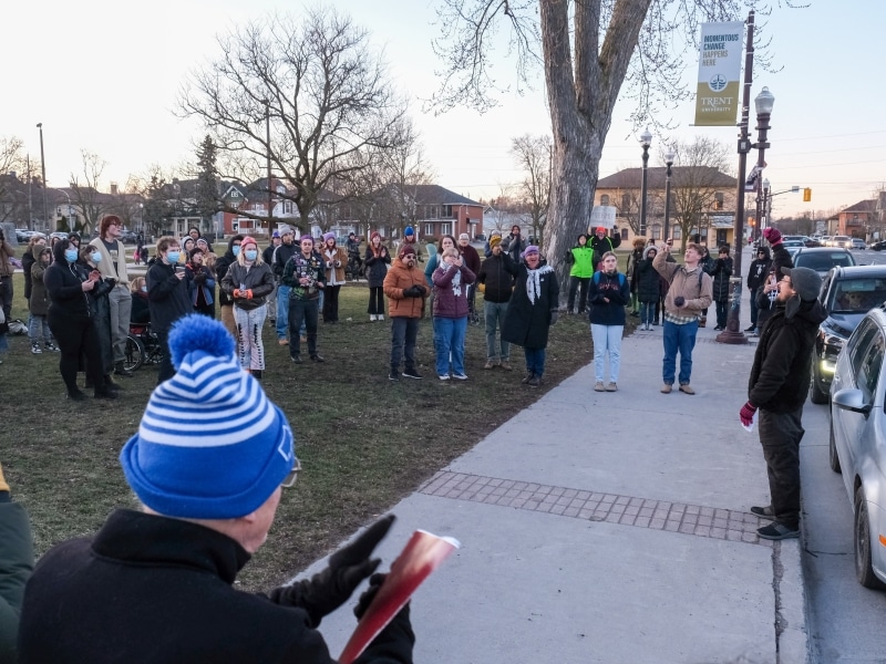 A group of people stand in Confederation Square, one of them smiles while holding a high sign that reads "you do not need a permit to do what is right."
