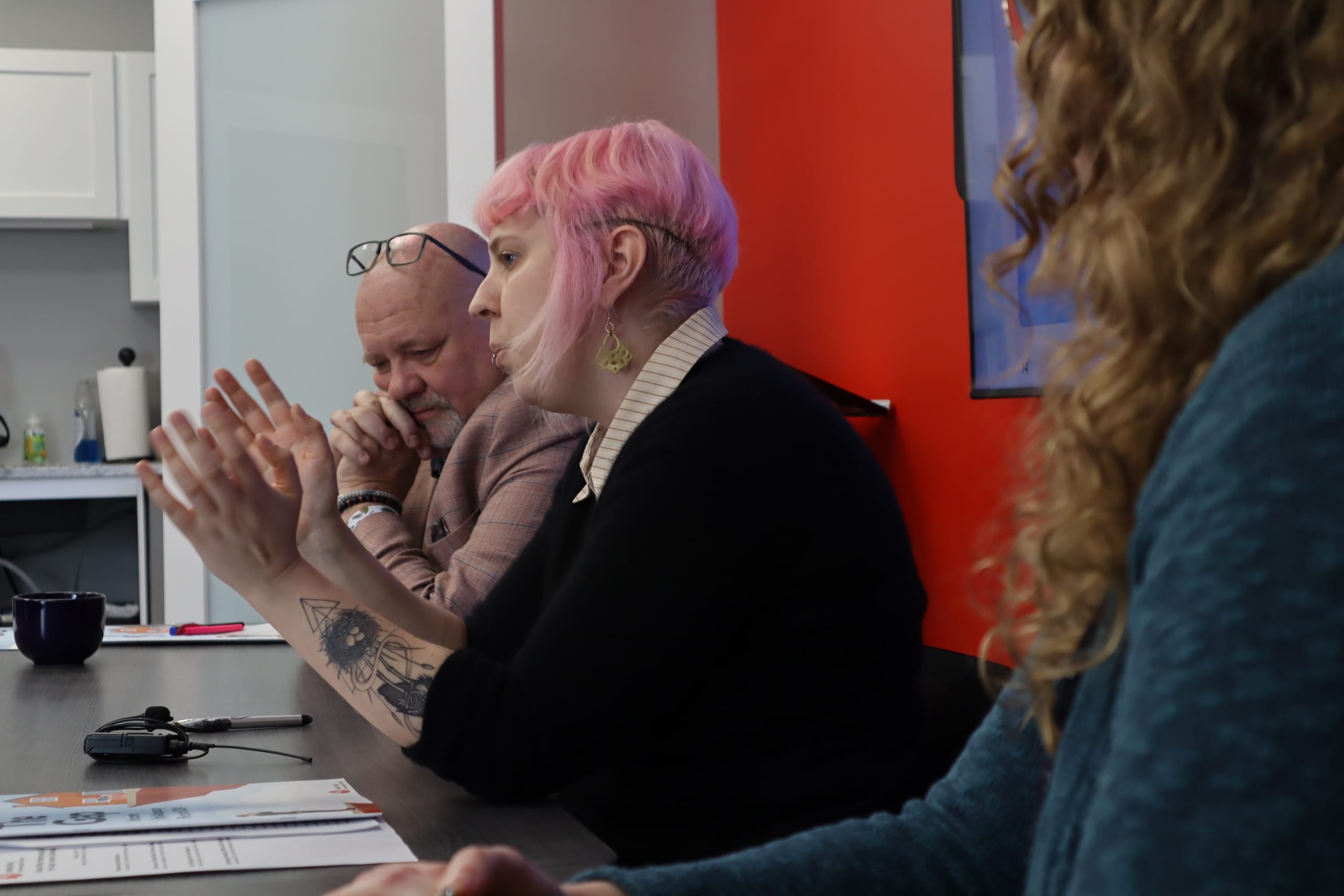 Photo shows three United Way staff members sitting in a row, as one of them (Elisha Rubacha) speaks to the media.