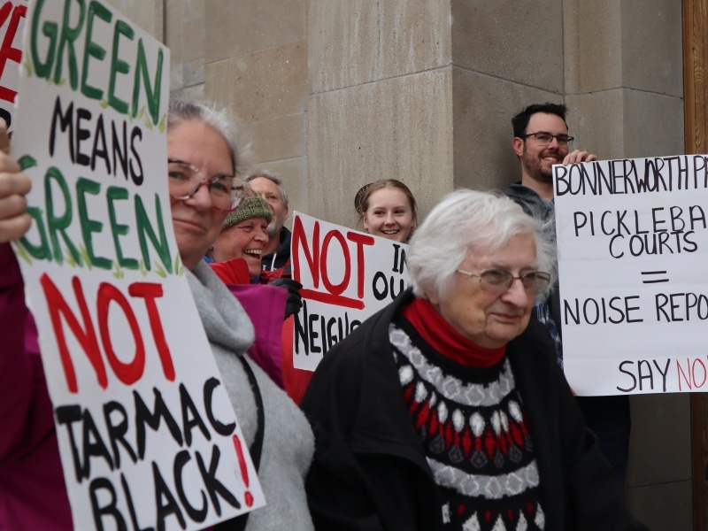 Photo shows several people standing on the front steps of Peterborough city hall, holding signs. One says "green means grean, not tarmac black!"