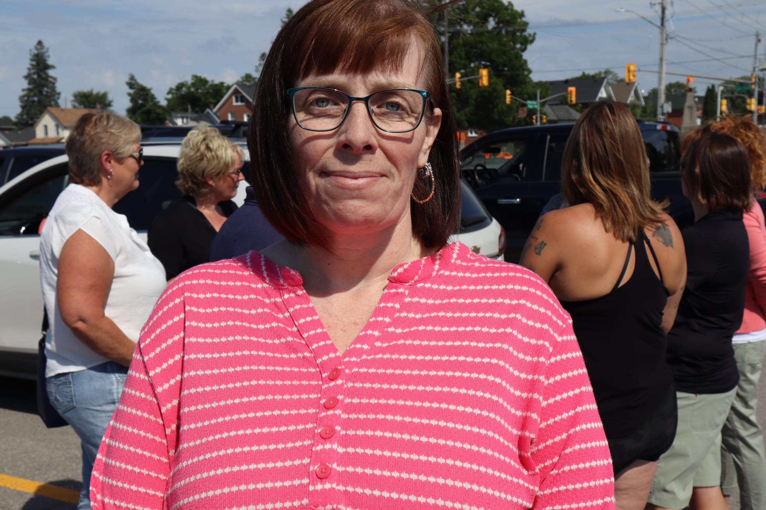 Photo shows Julie Chatten standing in front of a group of other bus drivers and monitors in a parking lot on a sunny day.