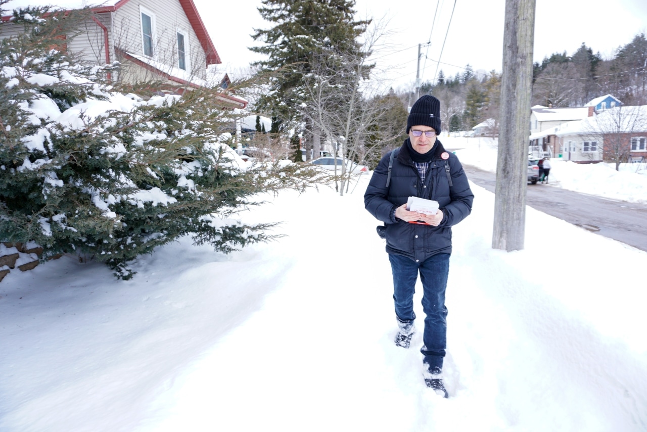Man walks down a snow-covered sidewalk holding Liberal election campaign pamphlets. 